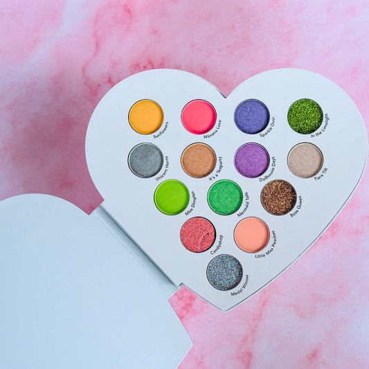 Heart-shaped makeup palette with colorful eyeshadows on a pink and white background