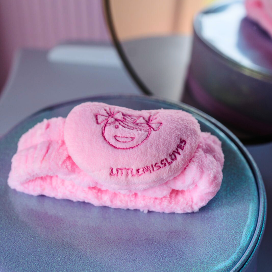 Pink plush cosmetic headband with 'LITTLE MISS LOVE' branding on a metallic surface.