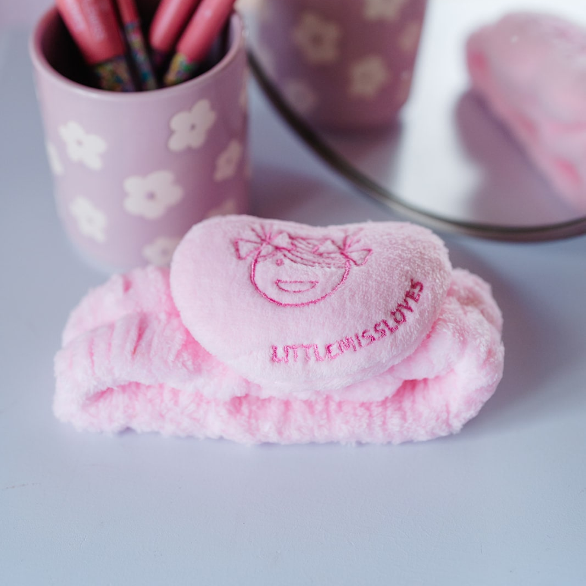 Pink heart-shaped soap with 'LITTLE MISS LOVES' text, next to a cup with pens on a light gray surface.