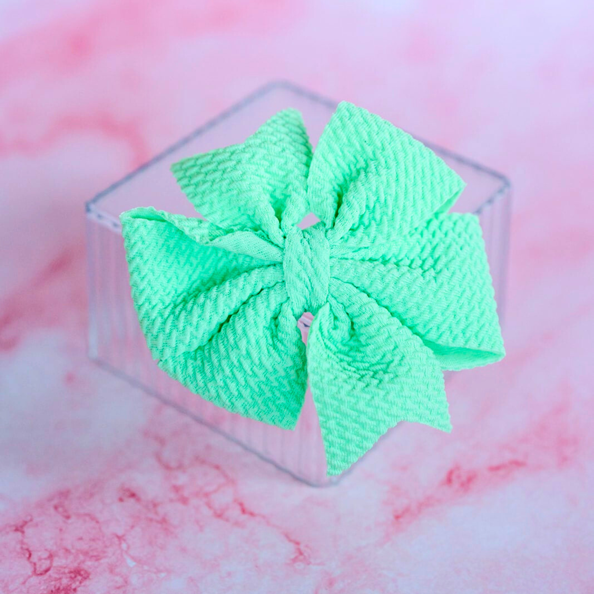 Green hair bow on a pink and white marble background