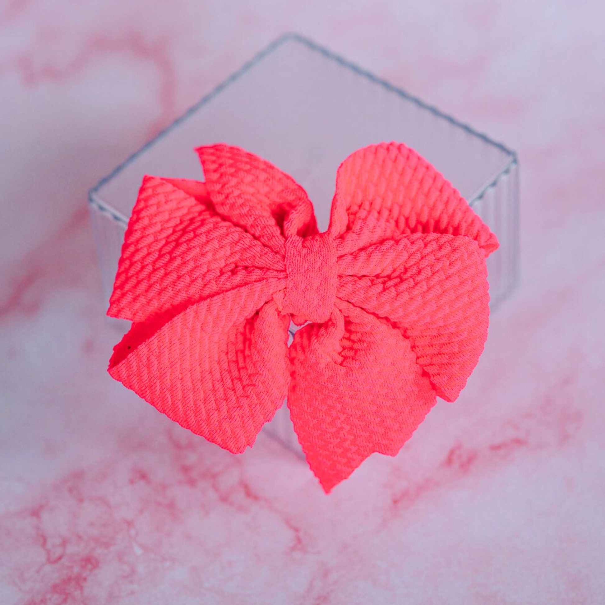 Pink bow on a clear stand against a pink marble background
