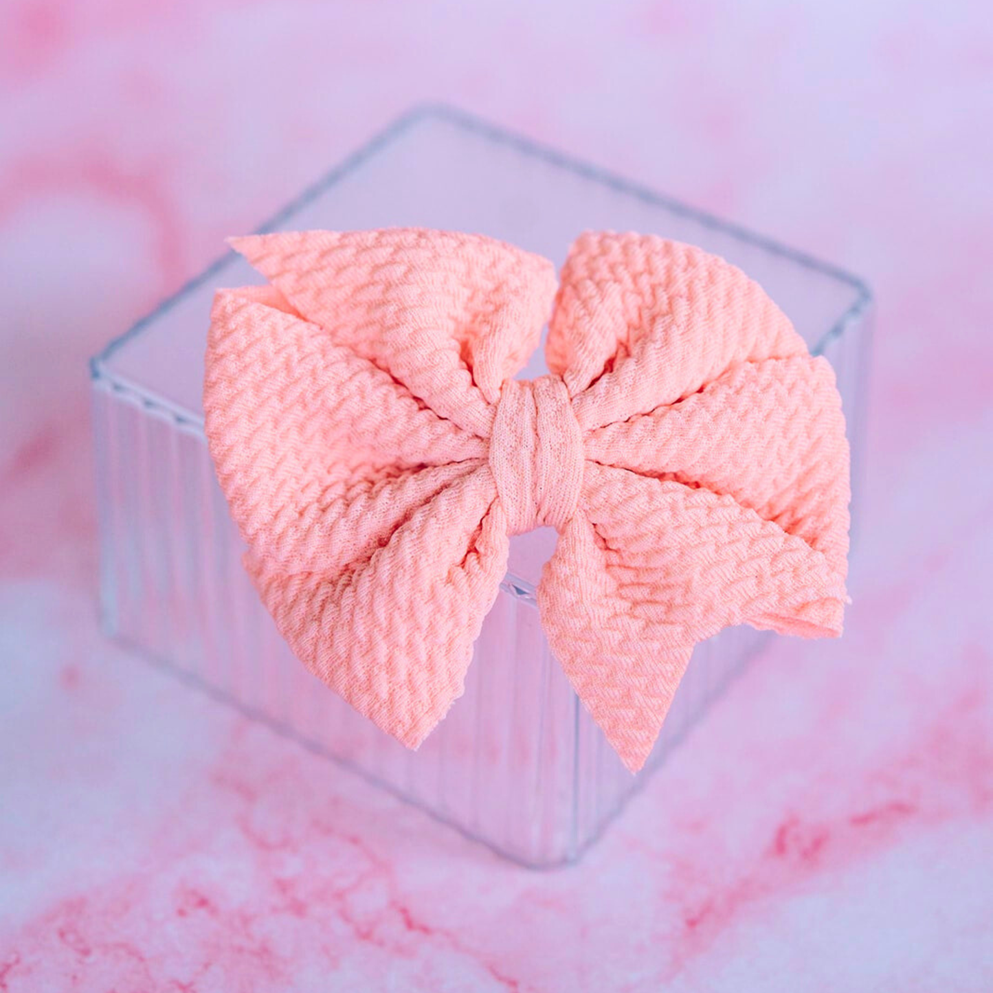 Pink knotted bow on a clear stand with a pink marble background