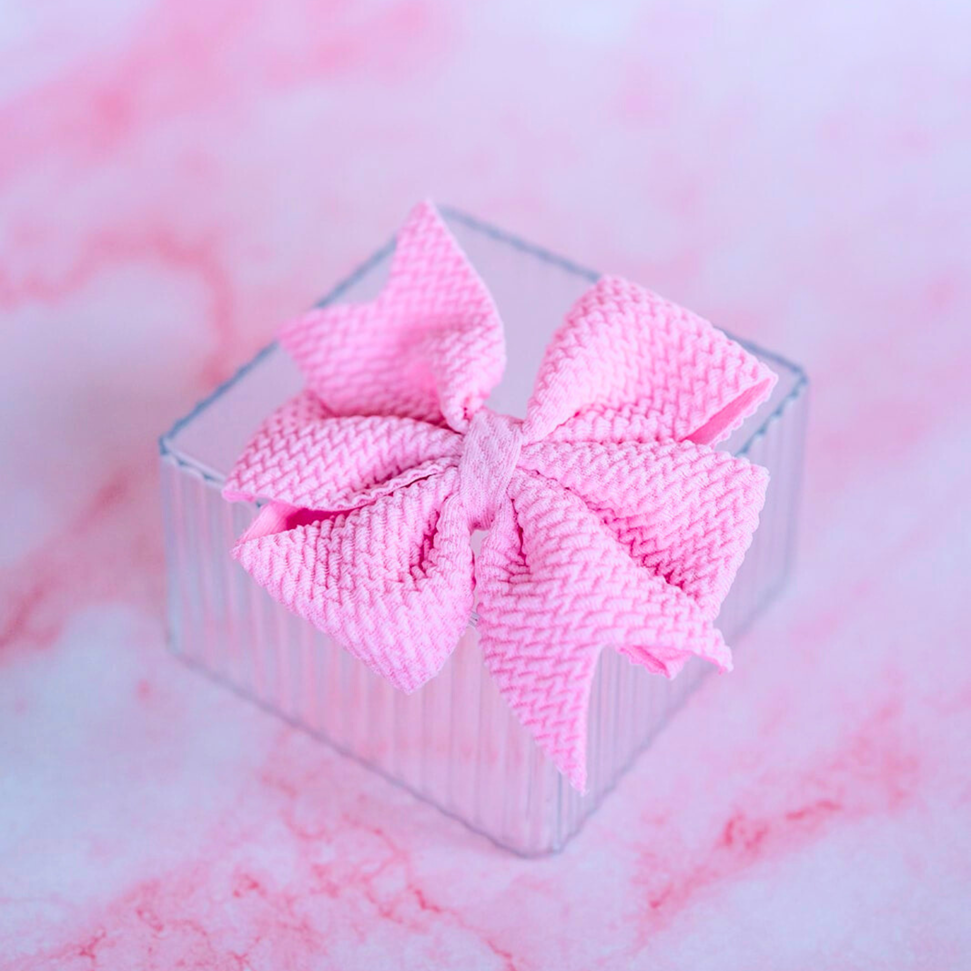 Pink textured bow in a clear box on a pink and white marbled background
