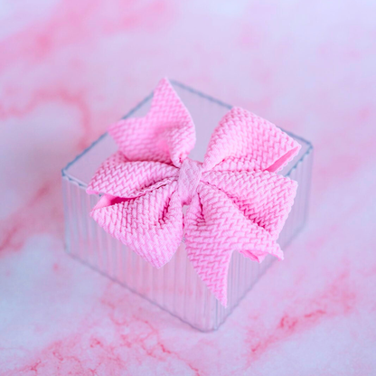 Pink textured bow in a clear box on a pink and white marbled background
