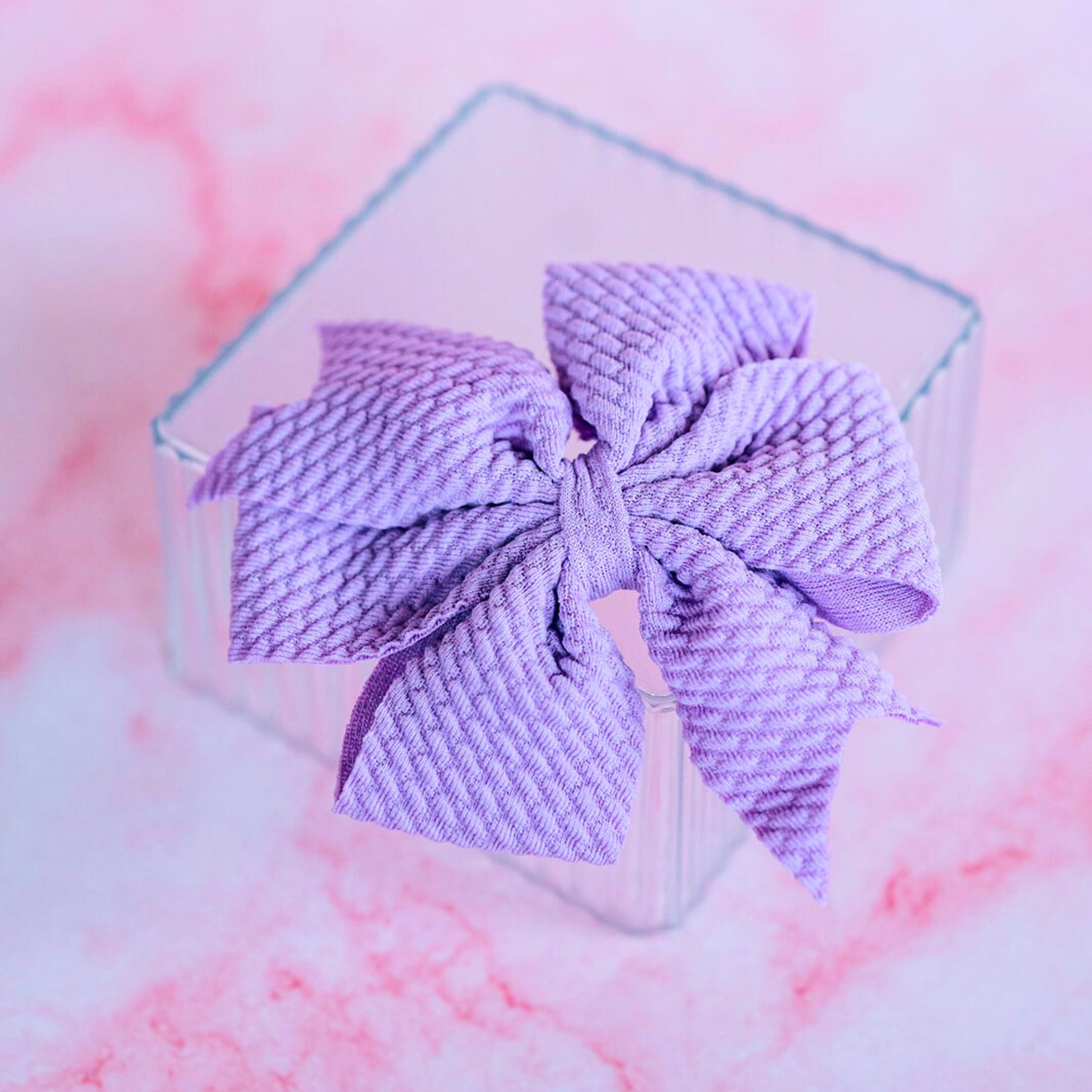 Purple textured bow in a clear cube on a pink and white background
