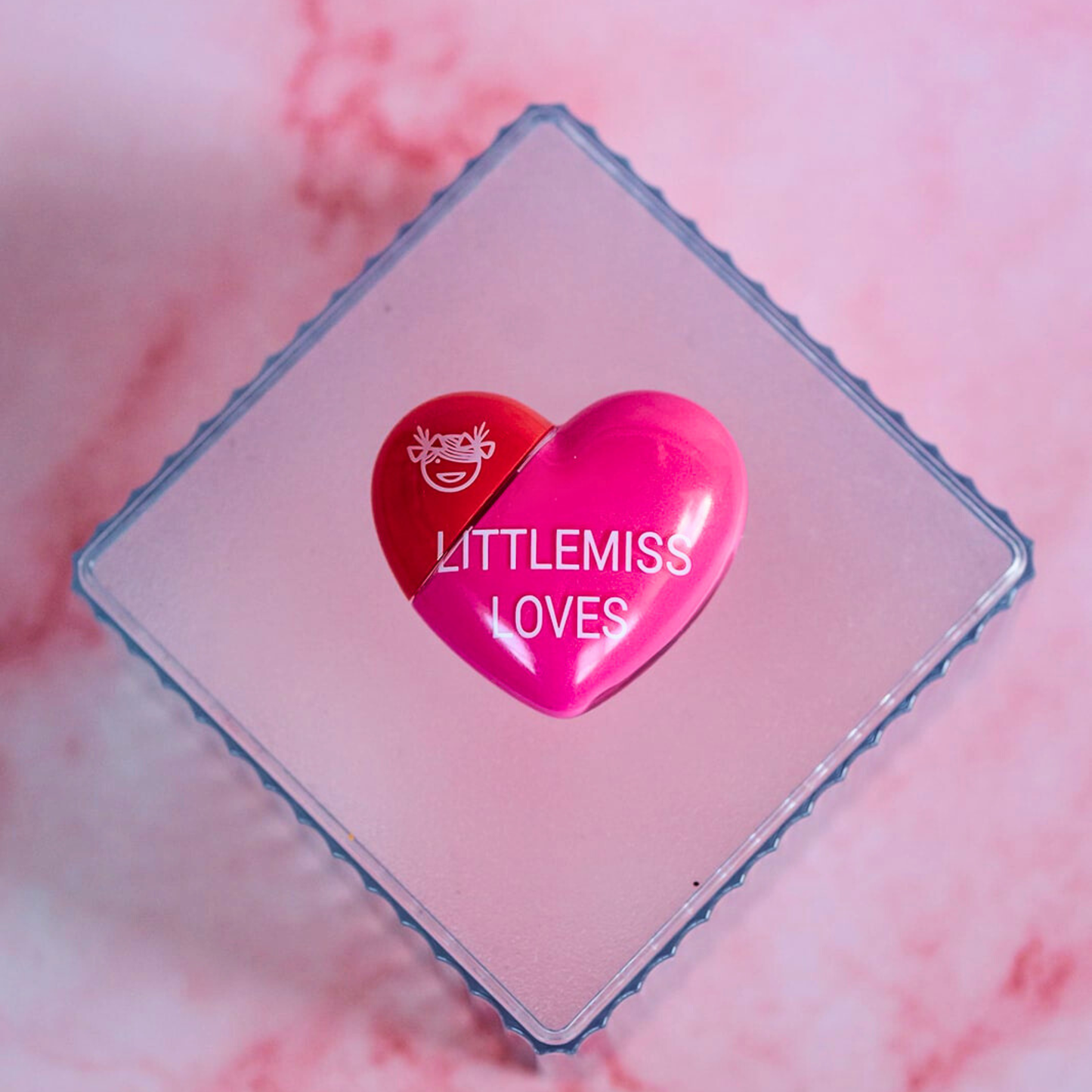 Heart-shaped product with 'LITTLEMISS LOVES' branding on a pink marble background