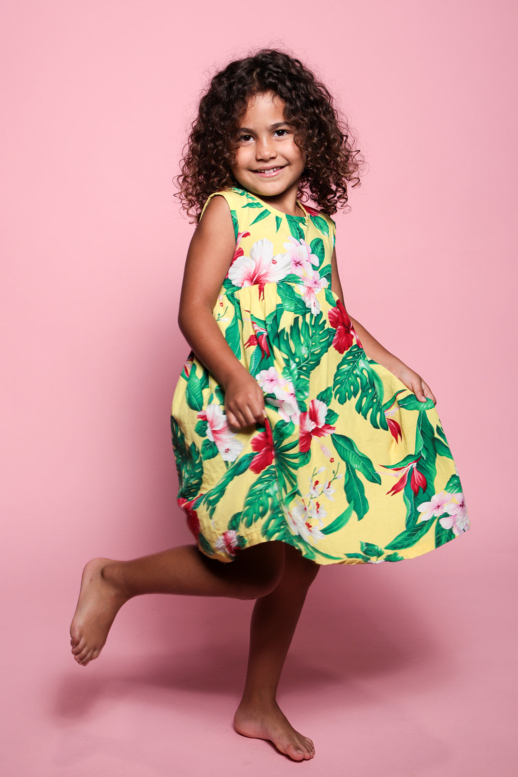 Young girl wearing a yellow floral dress against a pink background